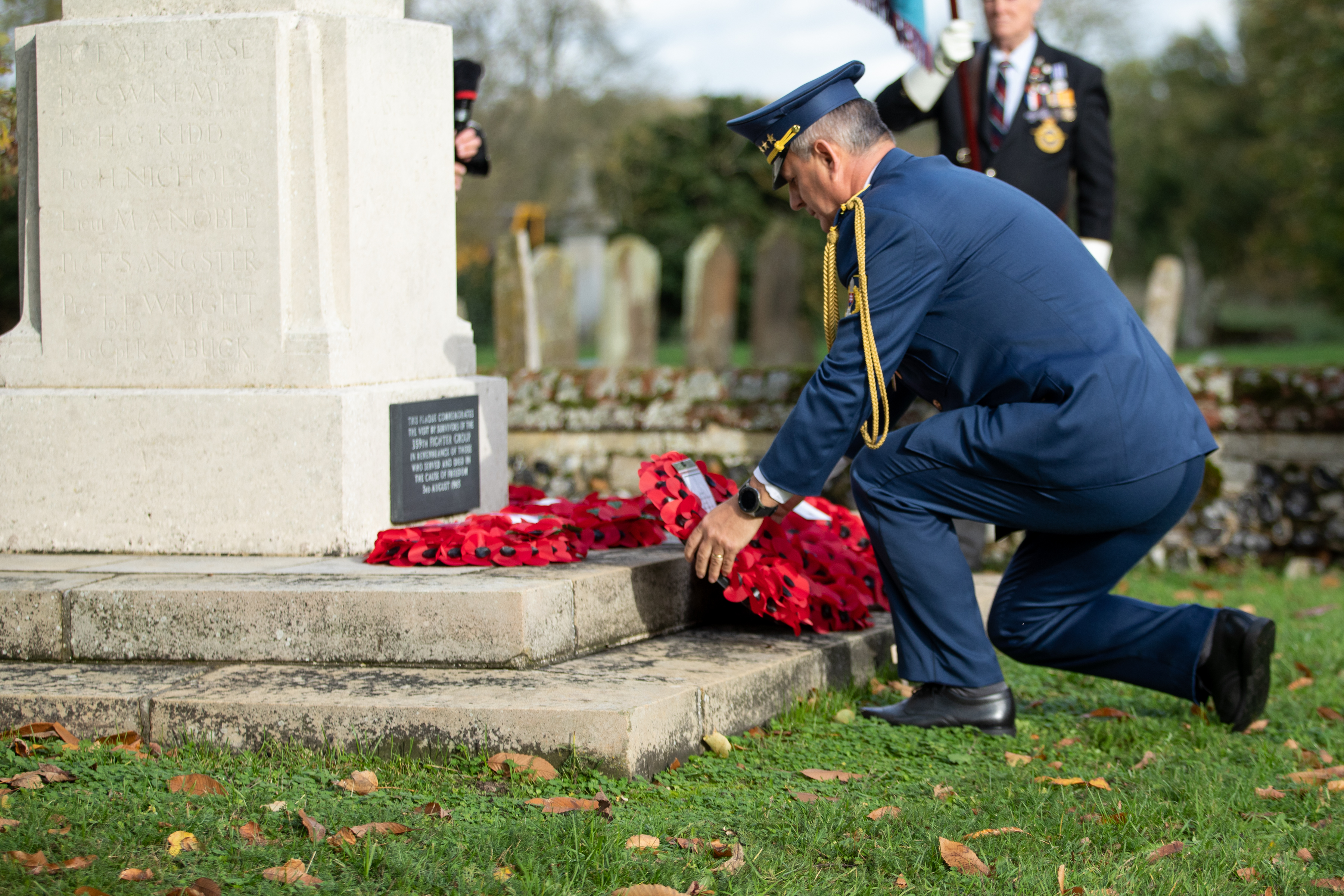 Image shows RAF aviator laying a poppy wreath by a memorial.